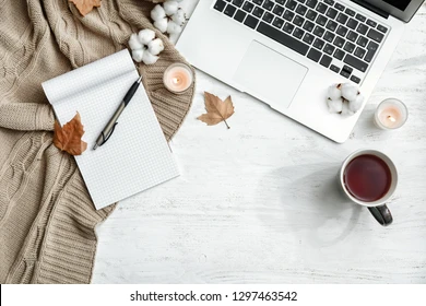 A flat lay of a cozy desk setup with a laptop, matcha latte, candles, and pastel notebooks — in soft lighting.